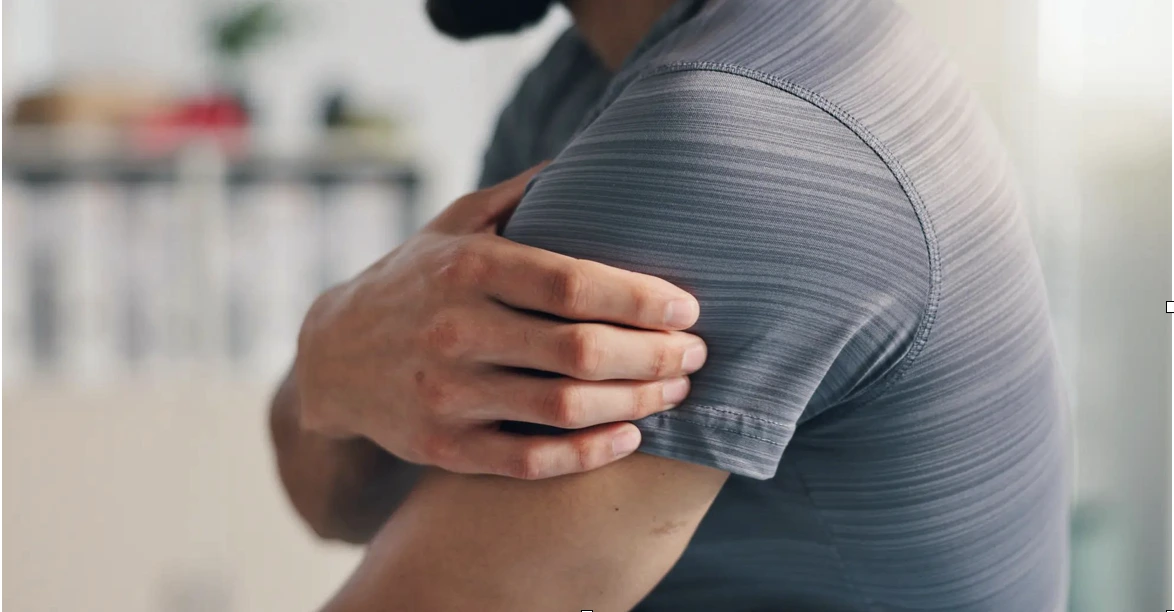 Someone who needs a rotator cuff repair holding their shoulder.
